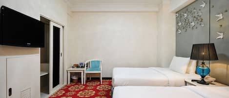 Quarto de hotel com duas camas, uma mesa, uma cadeira, uma televisão e um painel decorativo na parede.