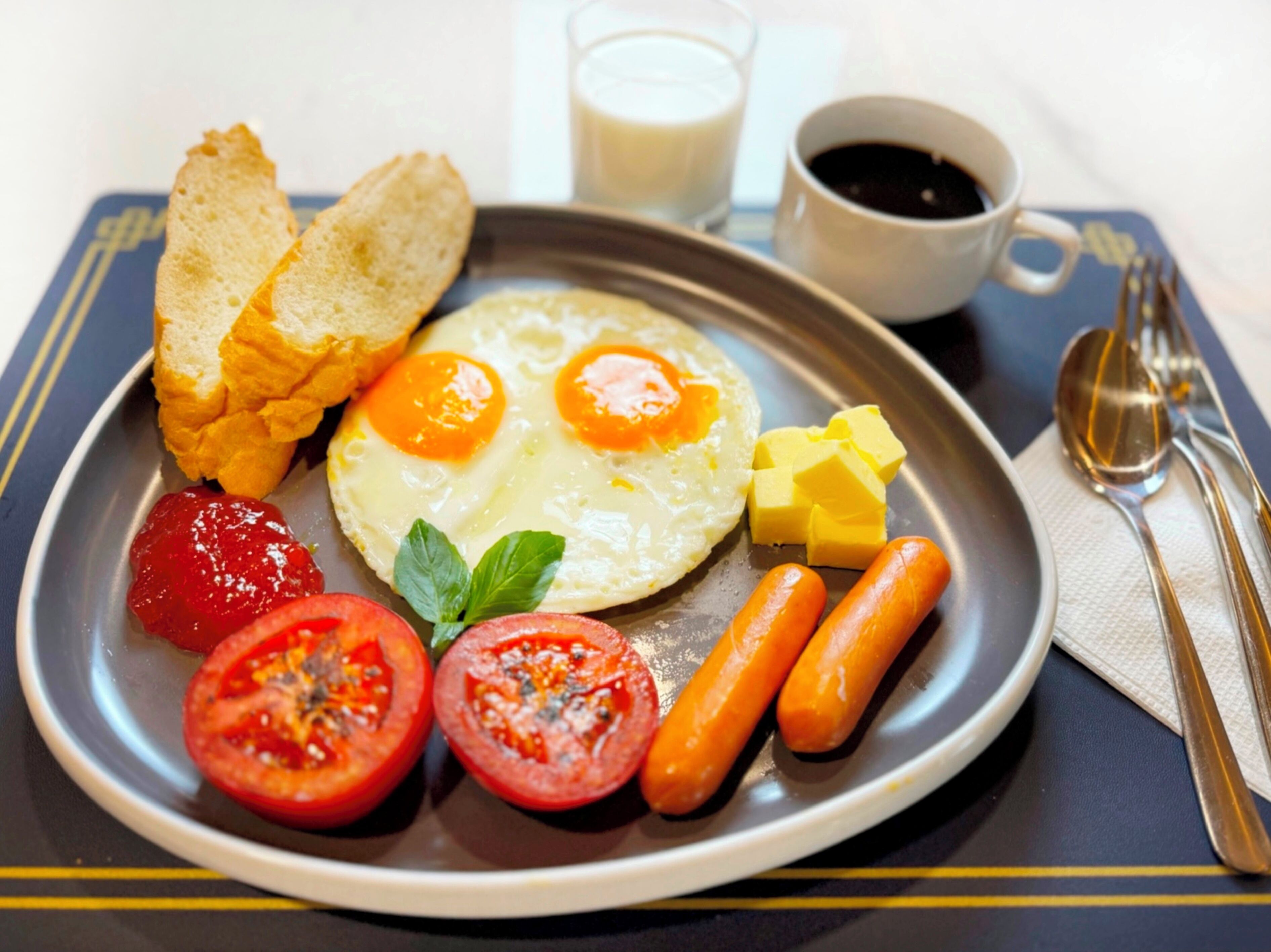 Une assiette de petit-déjeuner avec des œufs, des tomates, des saucisses, des toasts et du beurre.