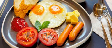 Ein Frühstücksteller mit Eiern, Tomaten, Würstchen, Toast und Butter.