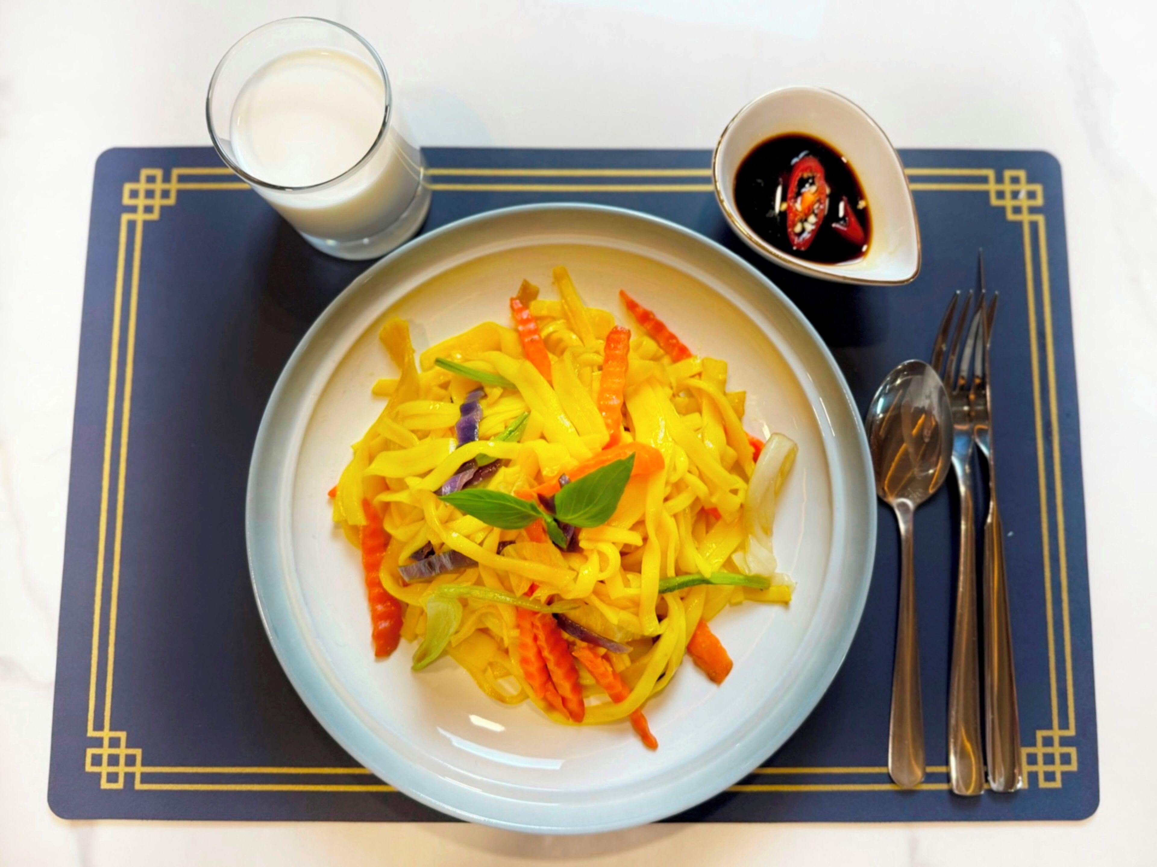 A plate of yellow noodles with vegetables on a blue placemat.