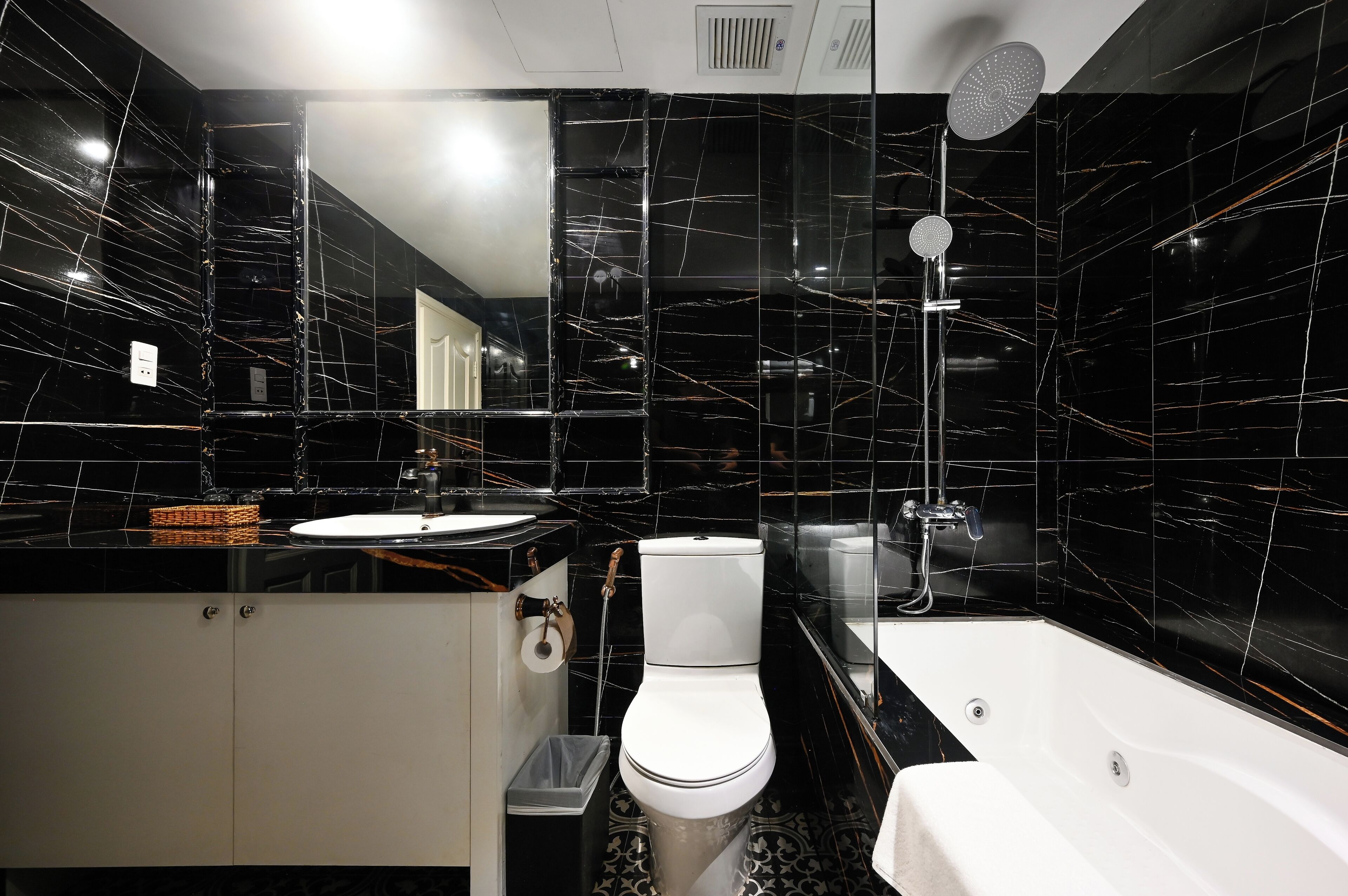 A modern bathroom with a black marble backsplash, a white toilet, a sink, and a bathtub.