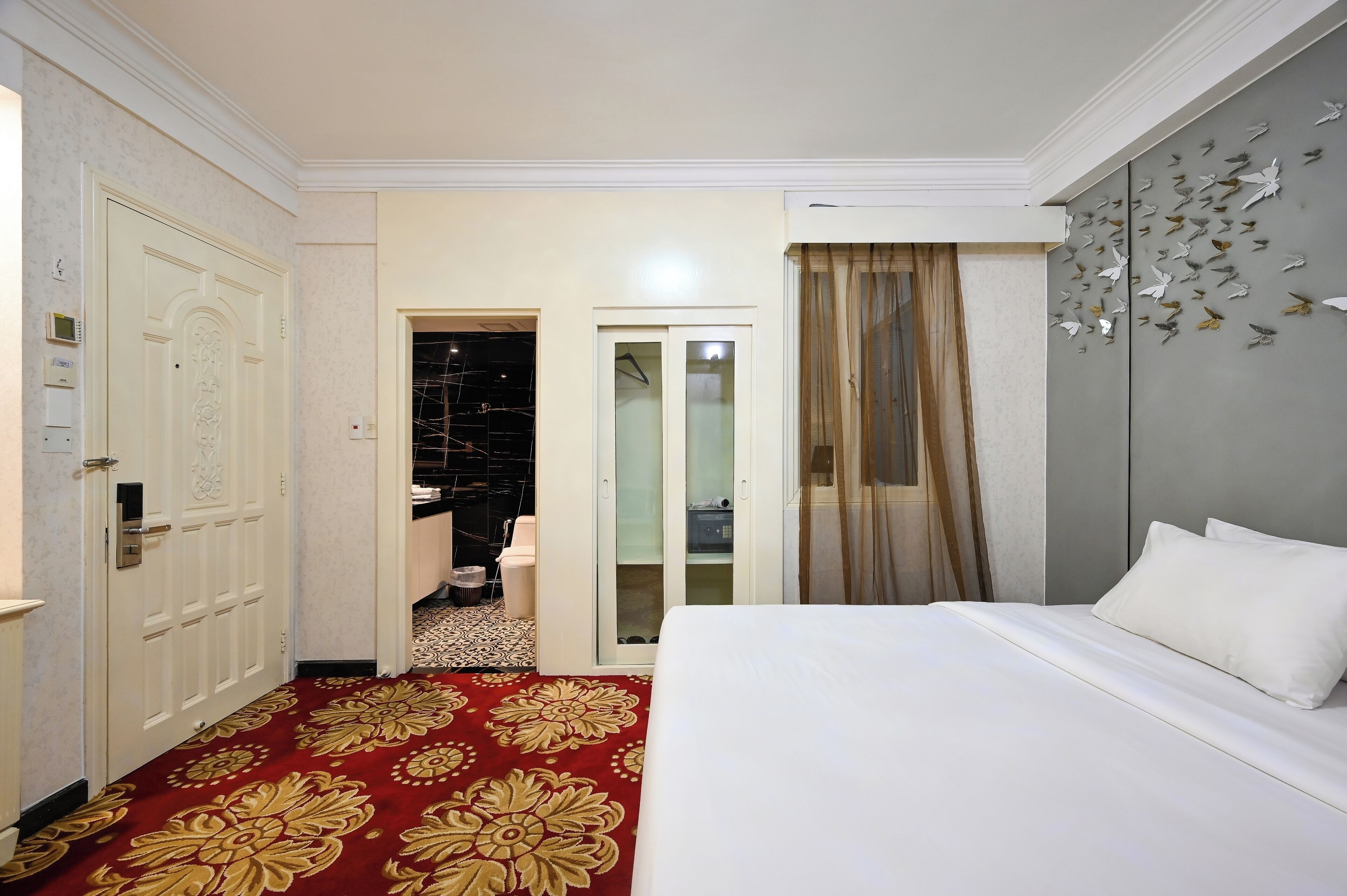 A hotel room with a large bed, a red carpet, a wardrobe, and a bathroom visible through an open door.