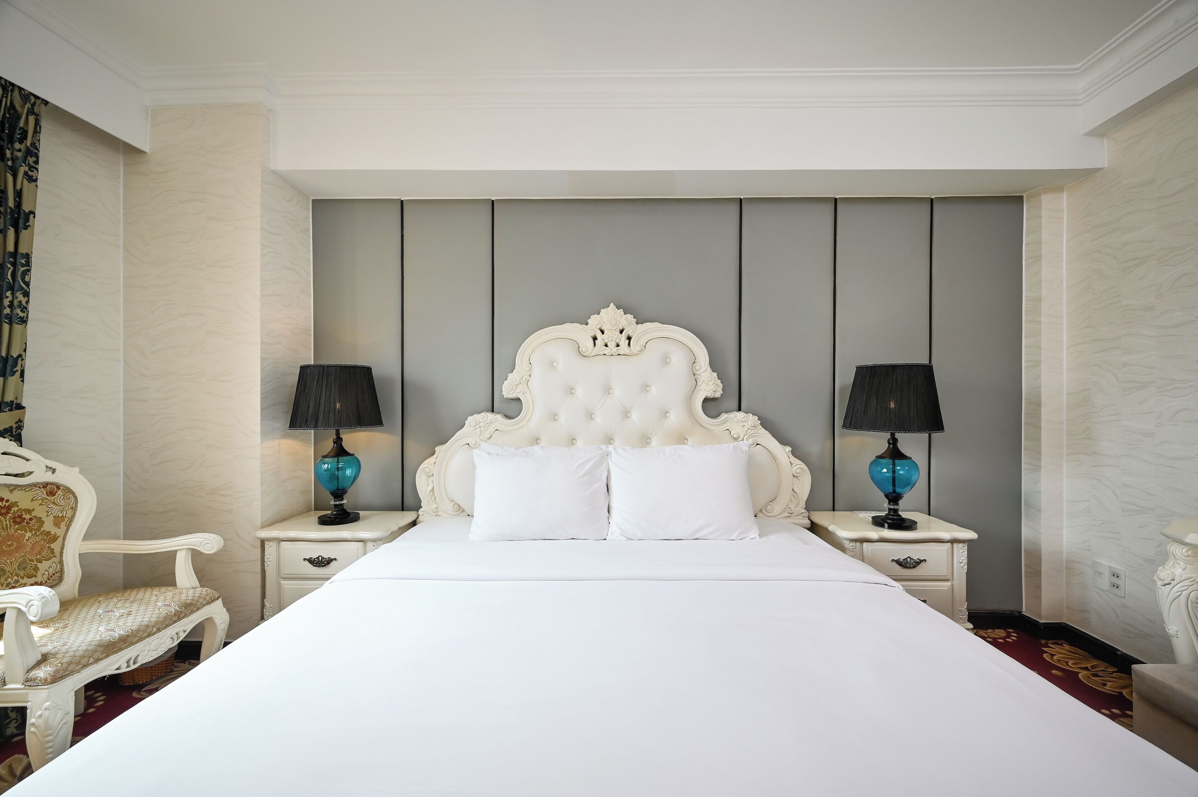 A large bed with a tufted headboard, two bedside tables with lamps, and a chair.