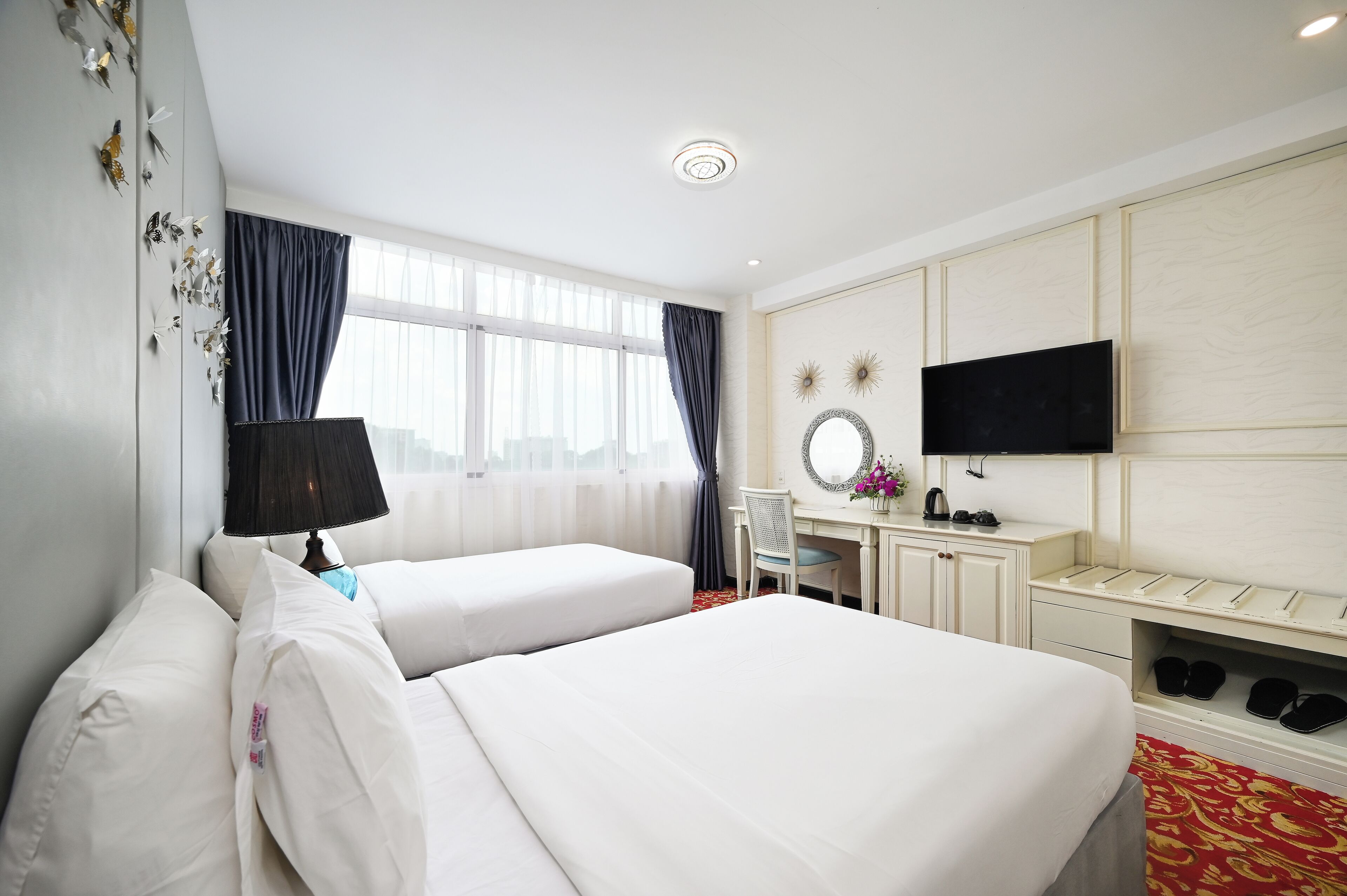 Ein Hotelzimmer mit zwei Betten, einem Schreibtisch, einem Fernseher und einem Schuhregal.
