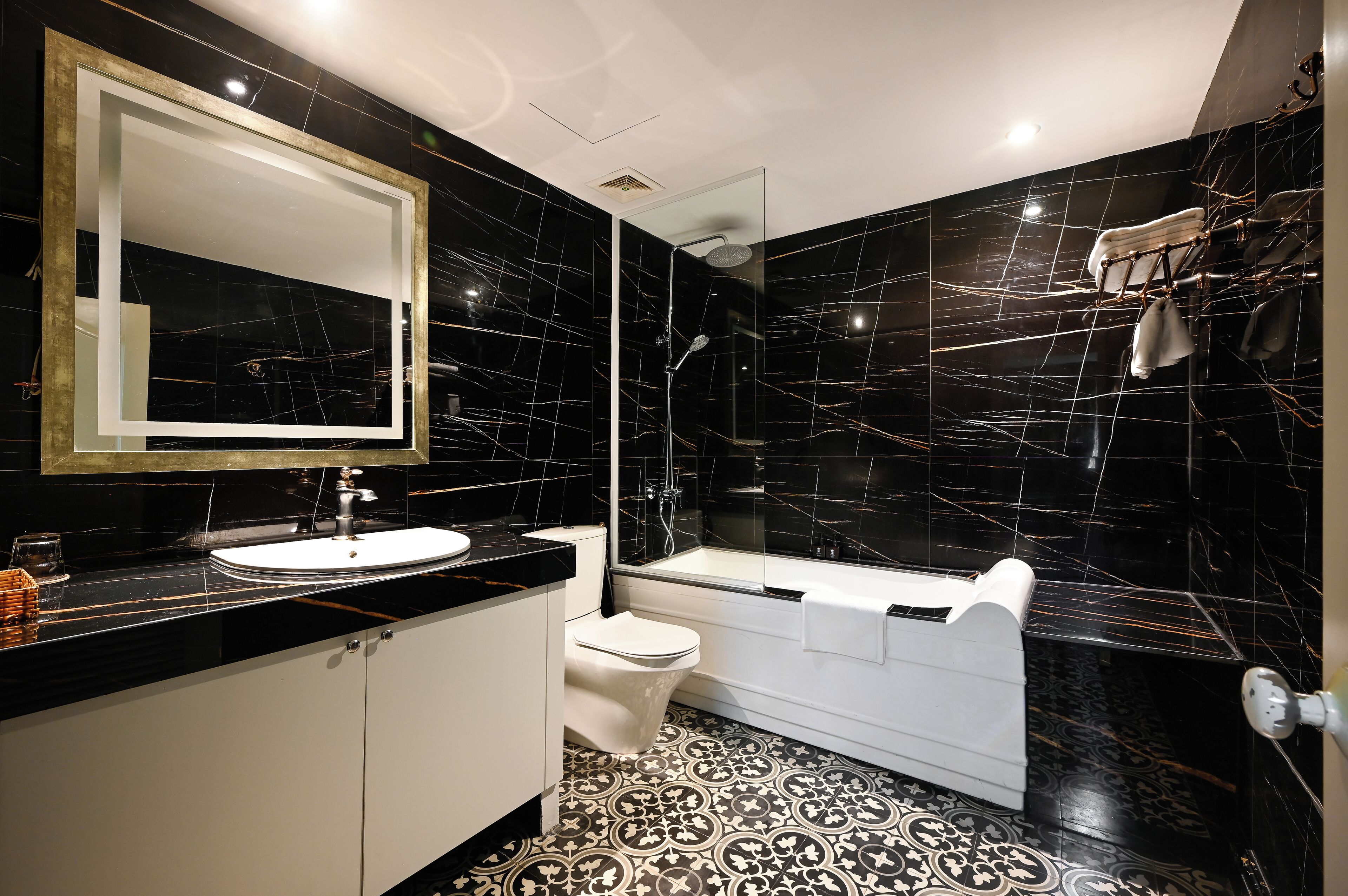 Ein modernes Badezimmer mit Schwarz-Weiß-Marmor-Design, einem großen Spiegel, einem Waschbecken, einer Toilette und einer Badewanne.