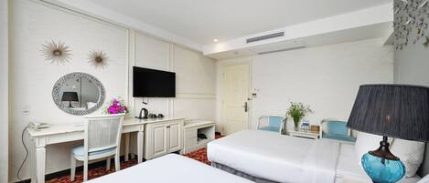 A hotel room with a bed, a desk with a chair, a TV, and a lamp.