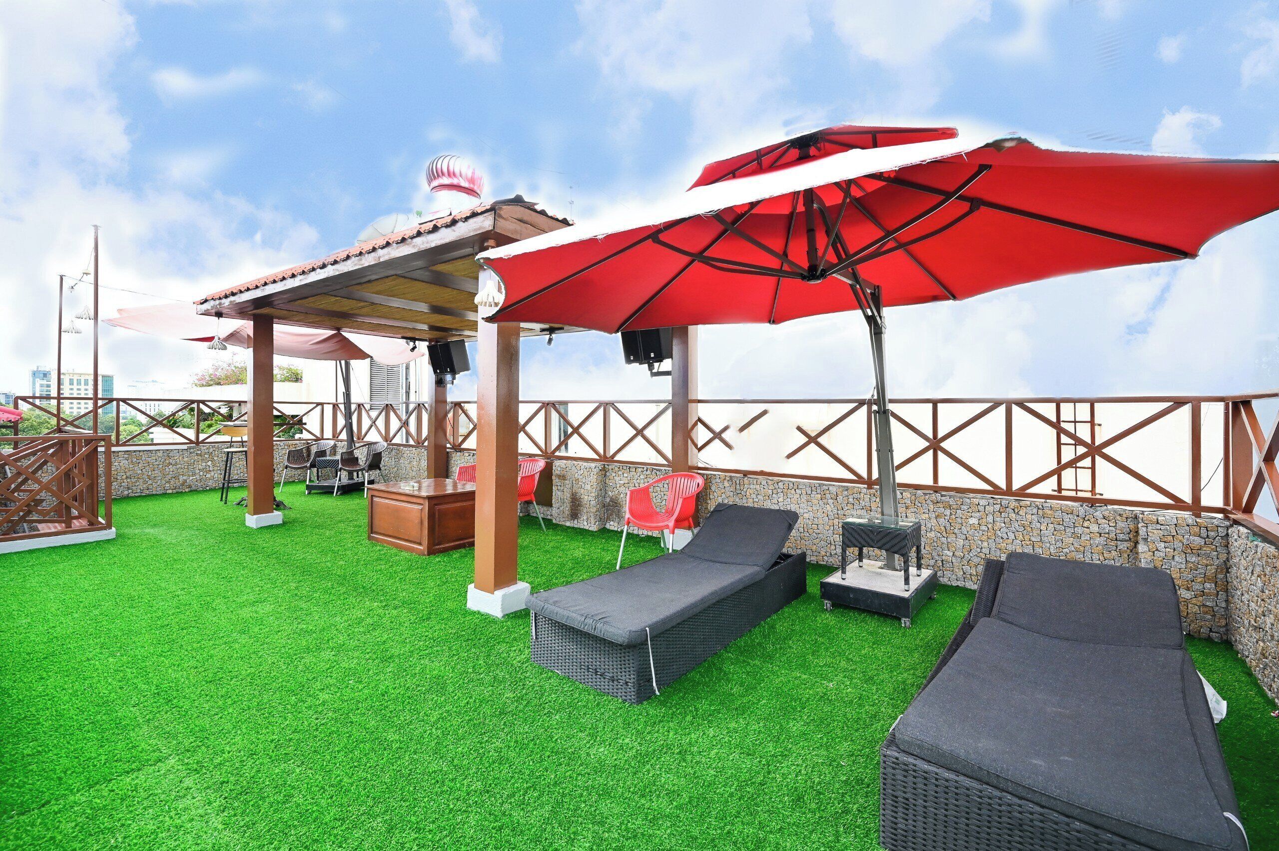 An outdoor patio with artificial grass, lounge chairs, and a red umbrella.