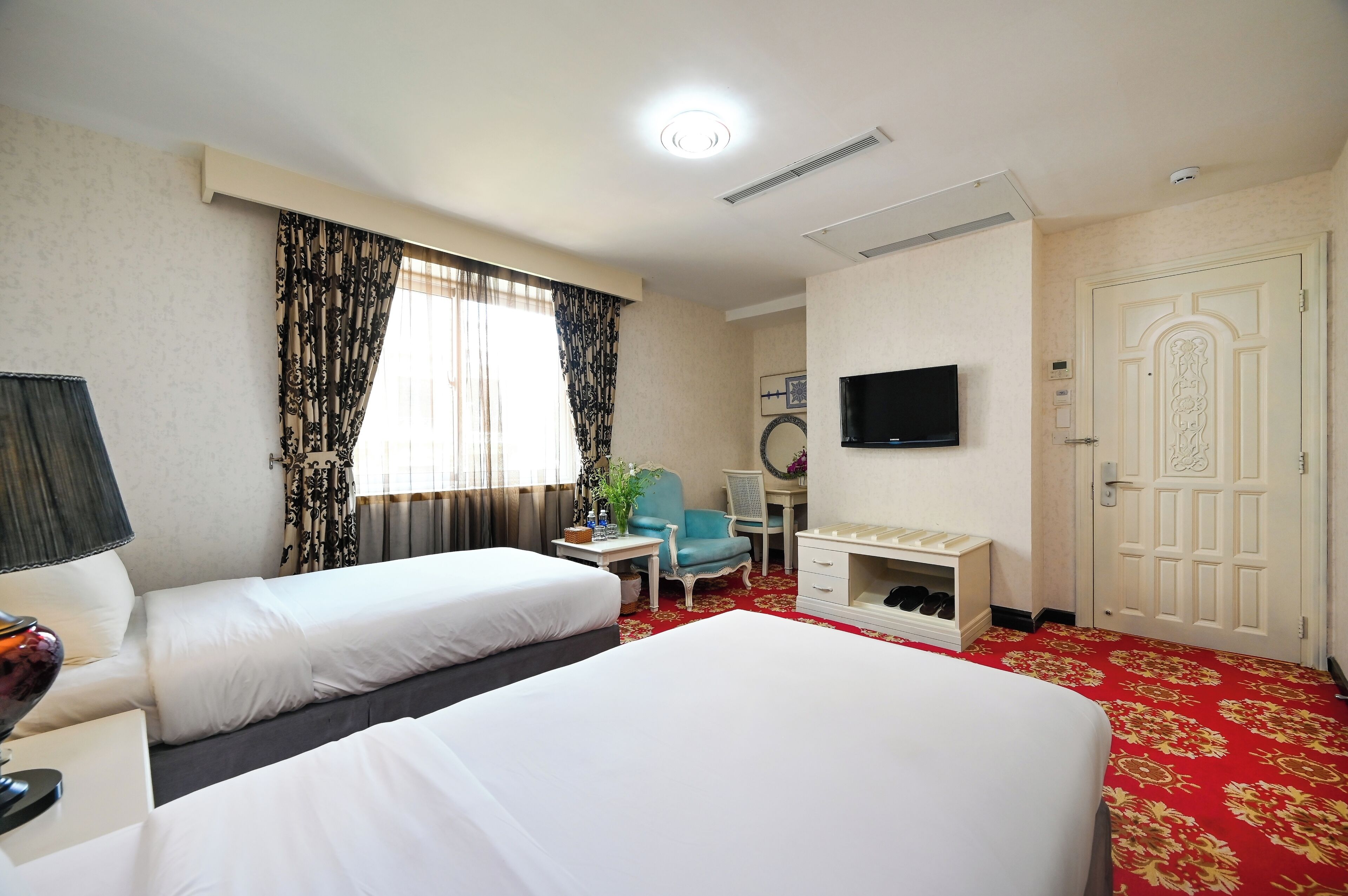 A hotel room with two beds, a desk, a chair, a television, and a wardrobe.