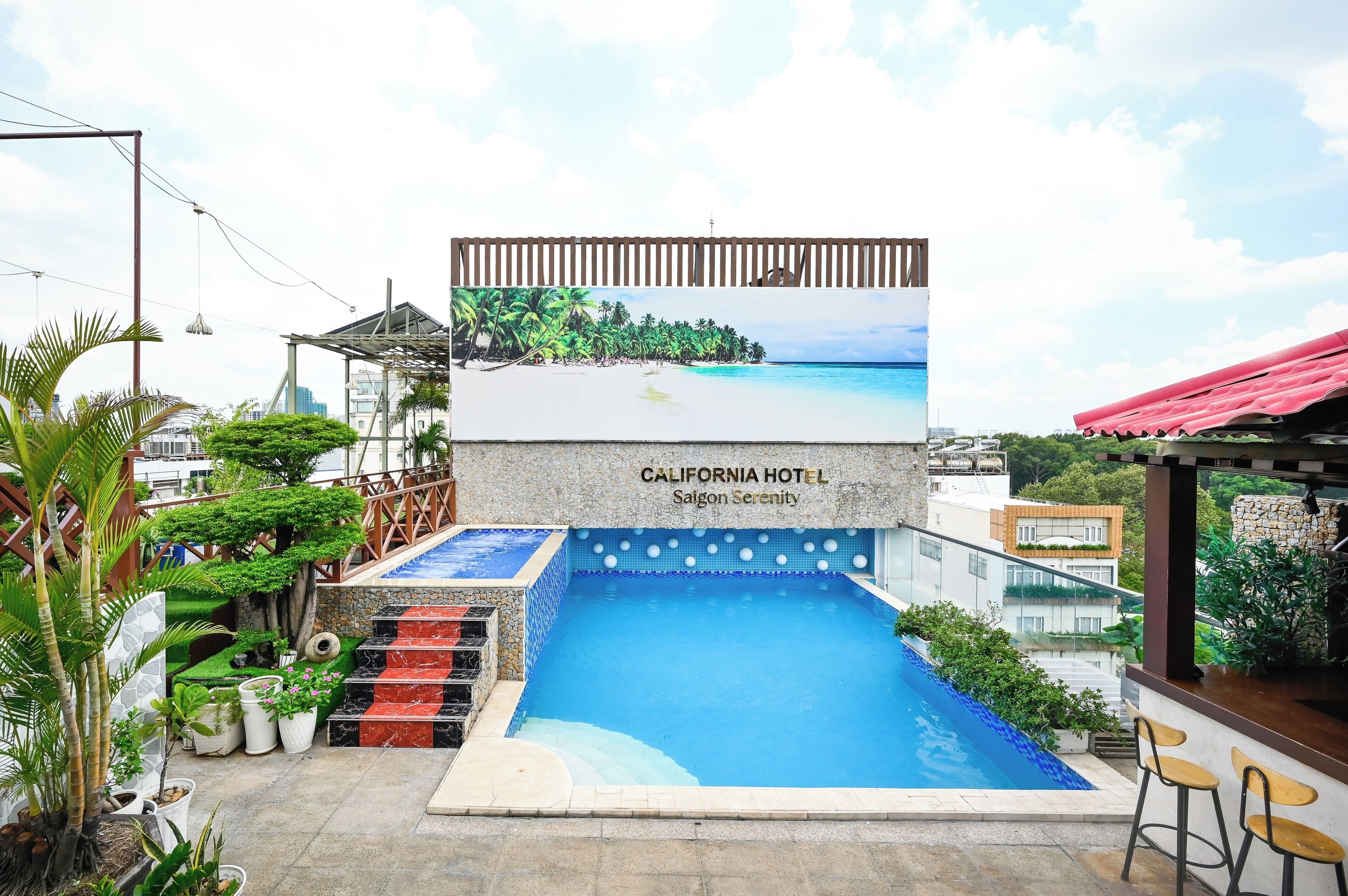 Zona de piscina con un mural de playa, un bar y un cartel de California Hotel Saigon Serenity.