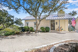 A stone building with a metal roof, a flag, and a small garden with a tree and shrubs. - White Buffalo Guest House I Wimberley Hills and Views, Romantic (Wimberley)