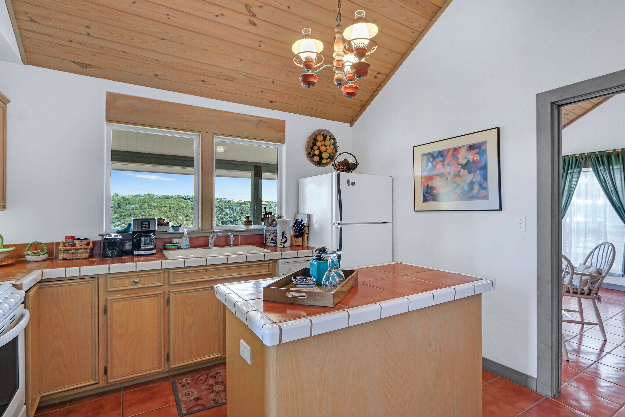 A kitchen with wooden cabinets, a central island, a refrigerator, and a window with a view.