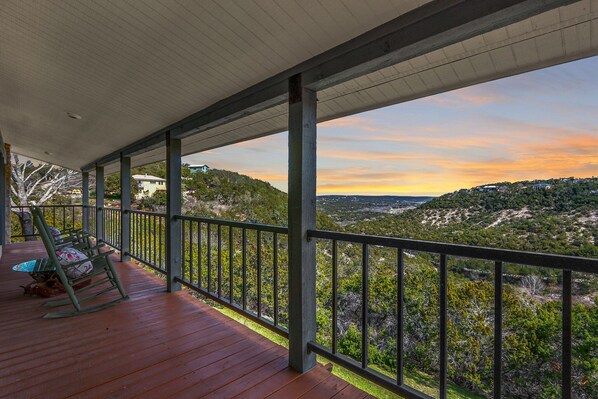 A covered outdoor area with a wooden deck, metal railing, and a view of a hilly landscape. - White Buffalo Guest House I Wimberley Hills and Views, Romantic (Wimberley)