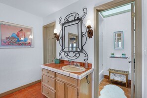 A bathroom with a white sink, wooden vanity, a decorative mirror, and a framed painting on the wall. - White Buffalo Guest House I Wimberley Hills and Views, Romantic (Wimberley)
