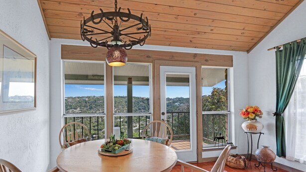 Un comedor con una mesa redonda de madera, sillas y una lámpara de araña metálica decorativa. Amplias ventanas ofrecen vistas al exterior.