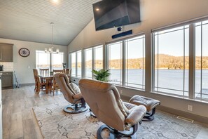 A spacious room with large windows, a flat-screen TV, a dining area, and two massage chairs. - Waterfront Lake of the Ozarks Home w/ Private Dock (Roach)
