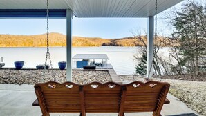 Een houten bank met hartvormige decoraties onder een overkapping, met uitzicht op een meer en bergen.
