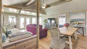 A spacious living area with a wooden floor, a large sofa, a dining table with wicker chairs, and a television. - Great for Groups: Oceanfront Surfside Beach Home! (Freeport)