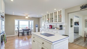 A kitchen with white cabinets, a dining area with a table and chairs, and a view of the beach through a large window.