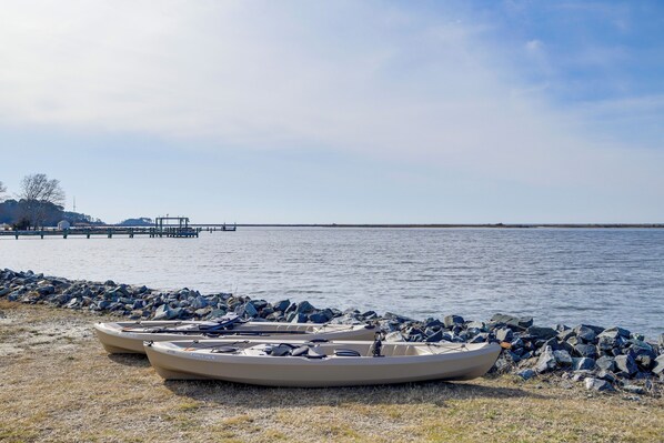 Two boats parked on a rocky shore by a calm body of water, with a pier extending into the water in the background.