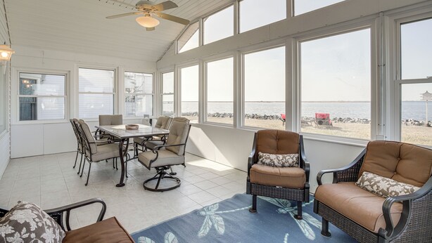 A sunroom with a dining table, chairs, and a view of the beach.