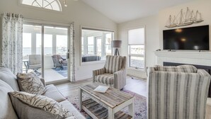 A spacious living room with a large window, a ceiling fan, a flat-screen TV, and a fireplace.