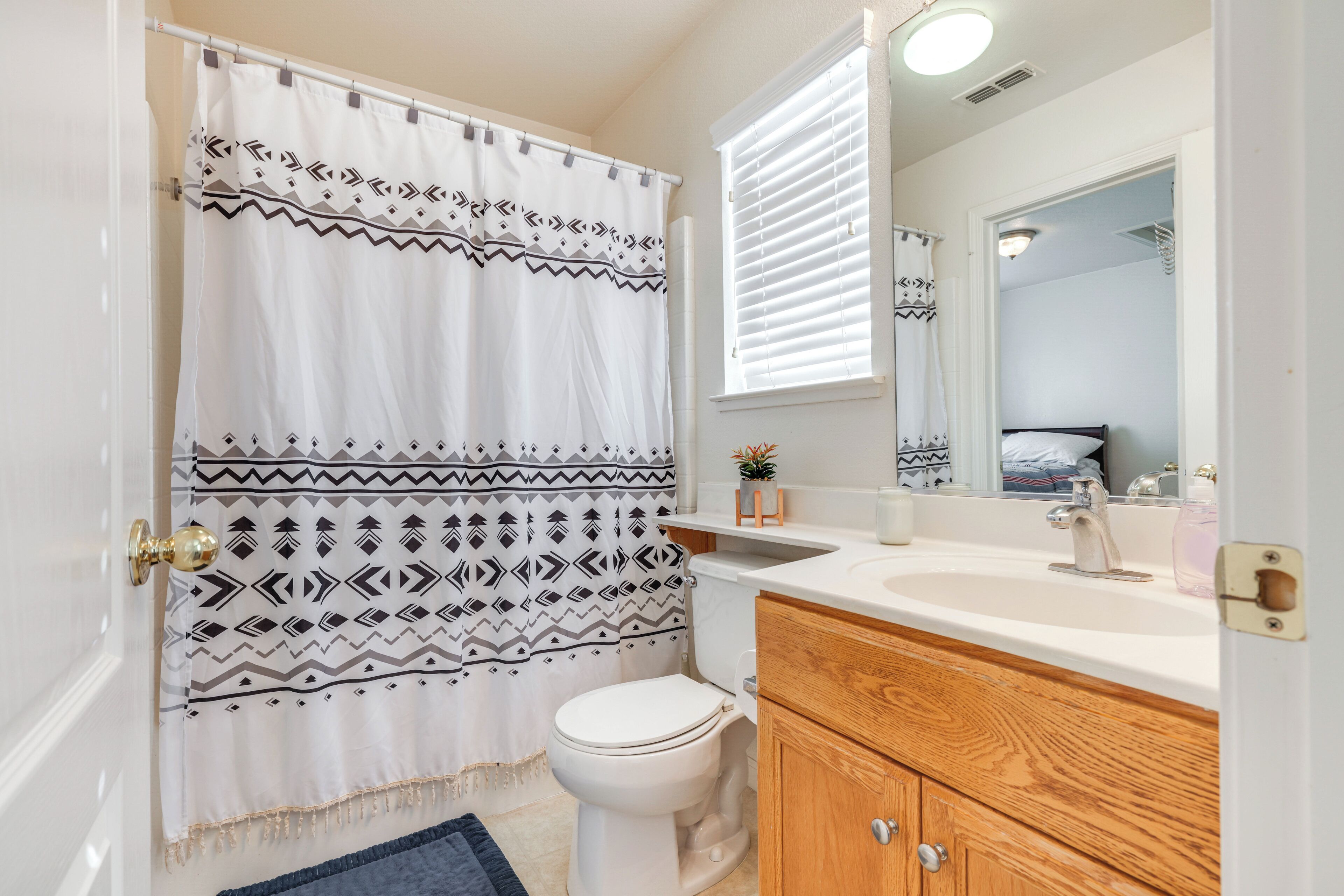 A bathroom with a shower curtain, toilet, sink, mirror, and wooden cabinet.