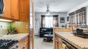 A kitchen with wooden cabinets, a stove, and a dining area with a black leather couch. - Spacious Turlock Home ~ 1 Mi to University! (Turlock)