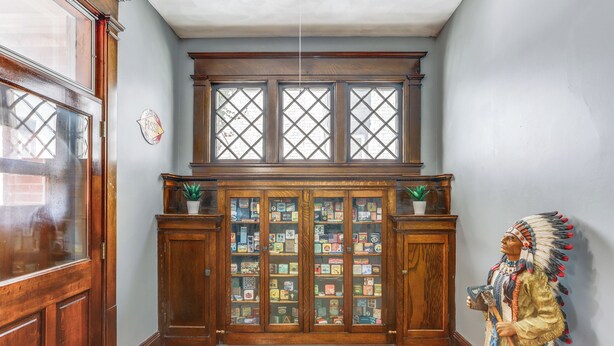 Een kamer met houten kastjes, een vitrine met diverse objecten, en een indiaanse sculptuur.