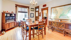 Een eetruimte met een houten tafel en stoelen, een kroonluchter, een boekenplank en een grote kaart aan de muur.