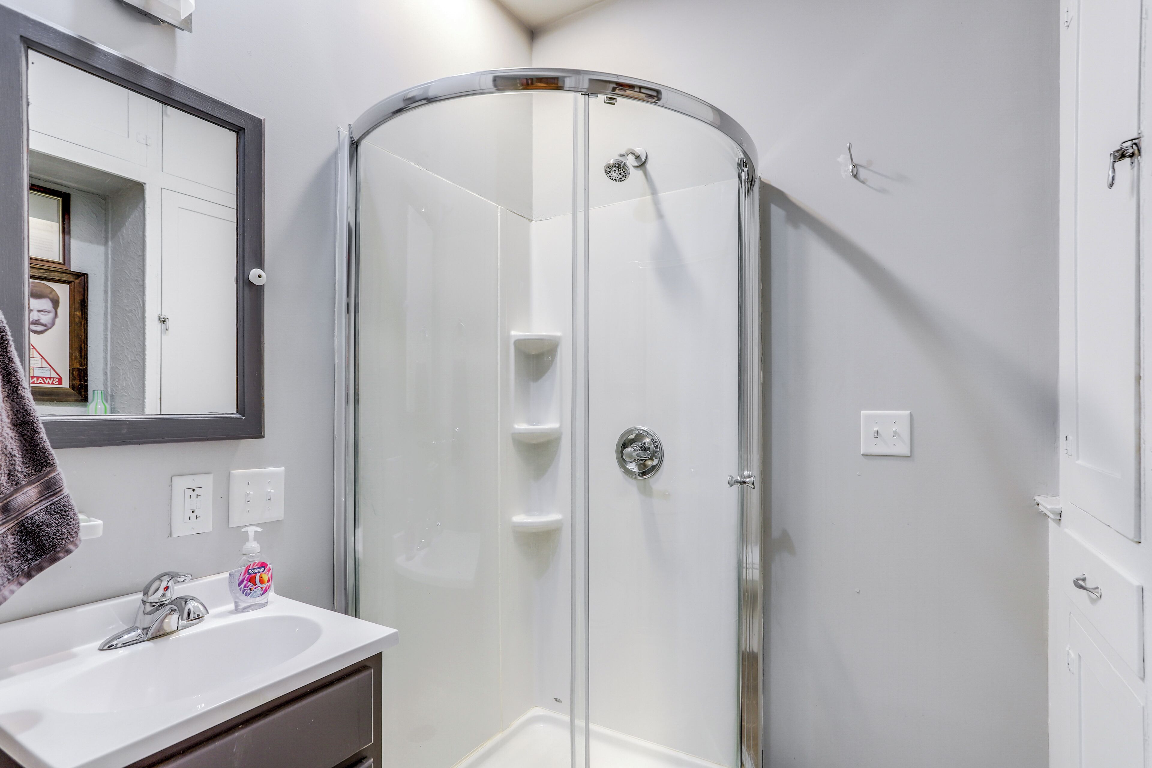 A modern bathroom with a glass-enclosed shower, a white sink with a mirror above it, and a towel hanging on the wall.