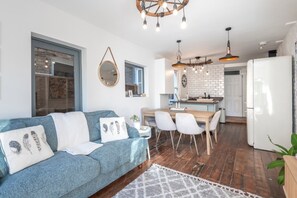 Un salon moderne avec un canapé bleu, un coin repas avec une table et des chaises en bois, et une cuisine avec des meubles blancs et un réfrigérateur.