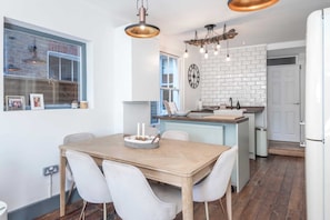 Une cuisine moderne avec une table à manger en bois, des chaises blanches et des luminaires suspendus.