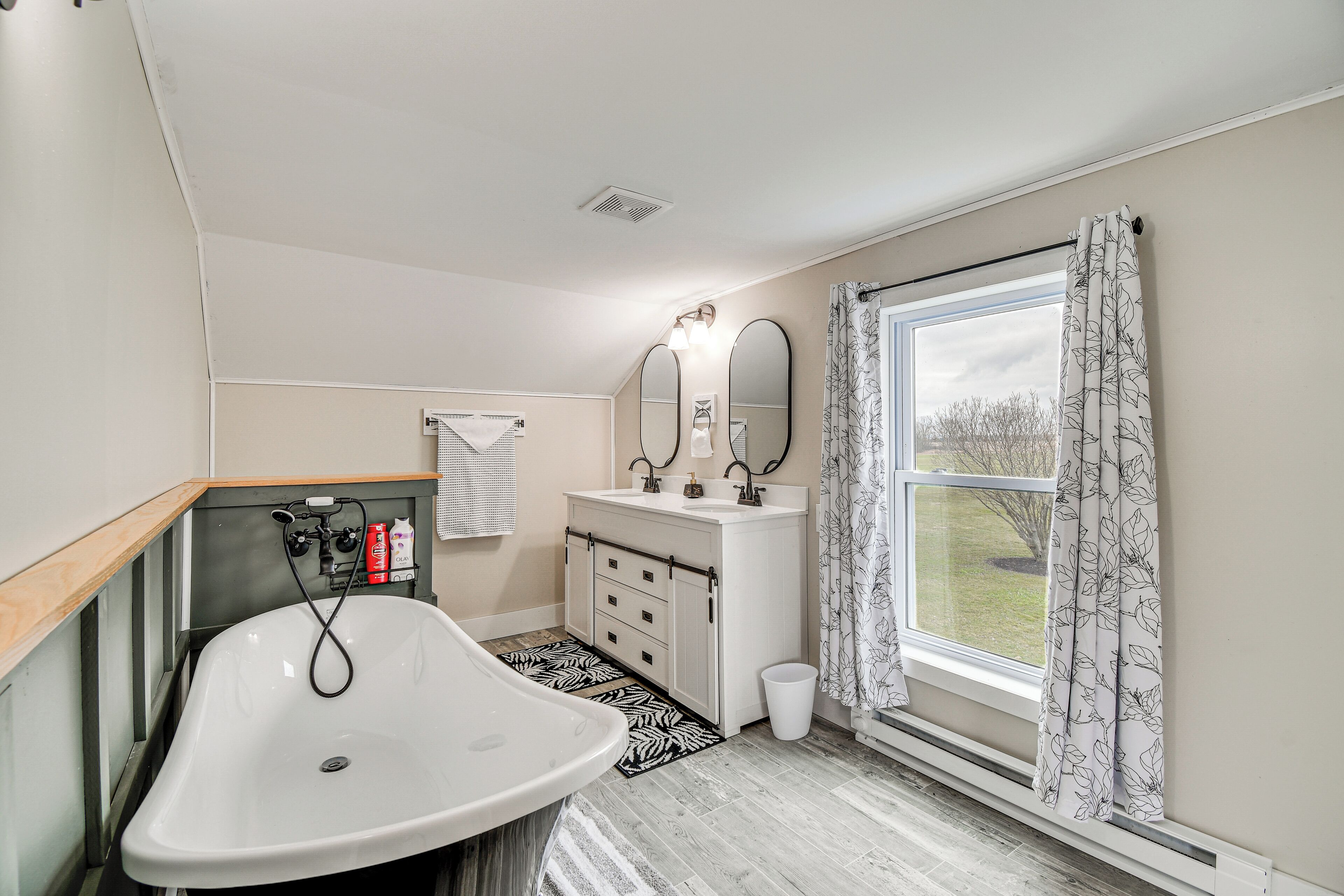 Une salle de bain avec une baignoire blanche, un lavabo avec un miroir et une fenêtre avec un rideau.
