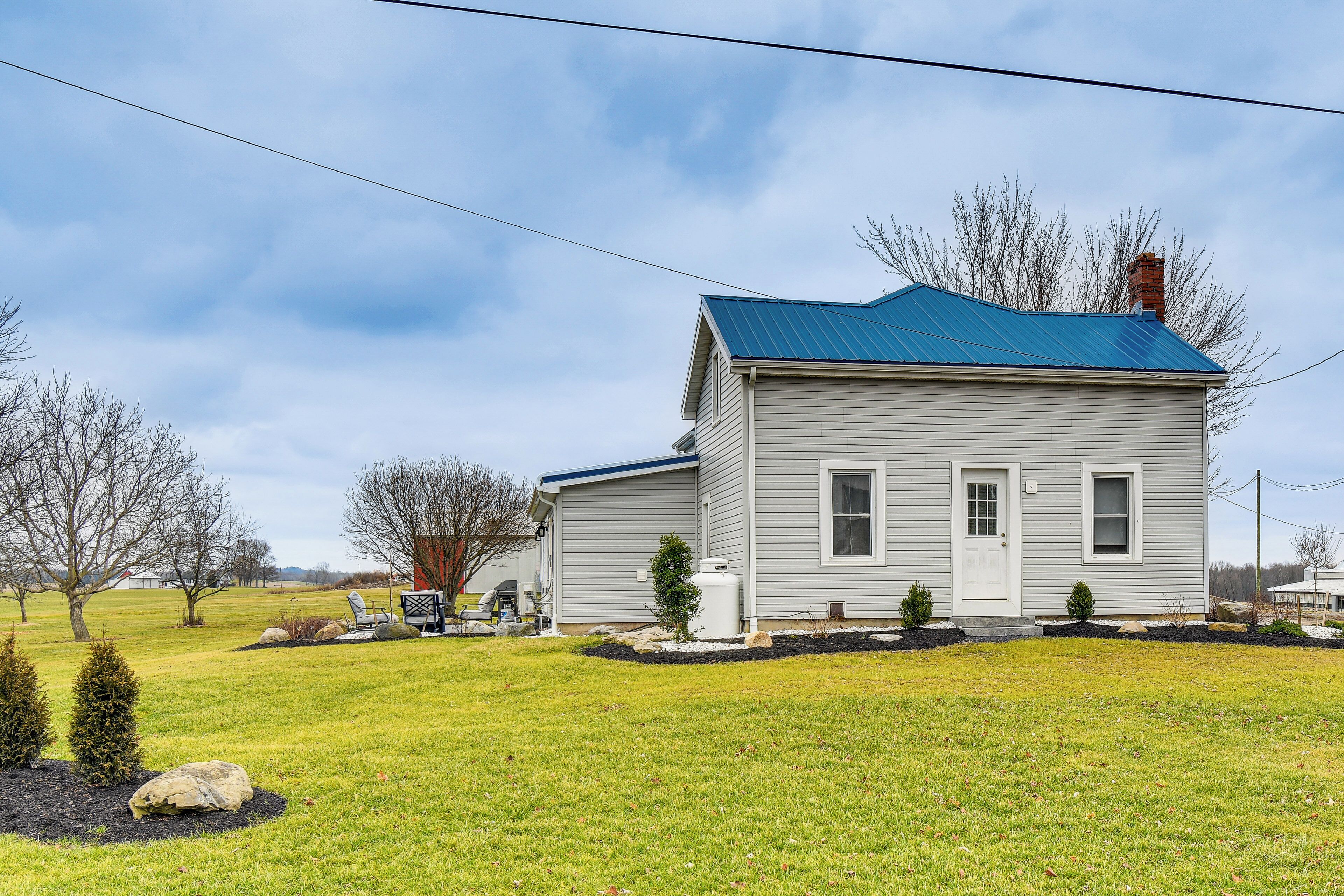 A two-story house with a blue roof, a front porch, and a small front yard with a lawn and a few trees.