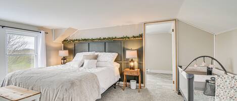 A bedroom with a bed, bedside tables, a nightstand, a crib, and a large mirror.