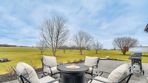 A patio with a round table and four chairs, a fire pit, and a grill. - Auburn Finger Lakes Farmhouse w/ Open Views! (Auburn)