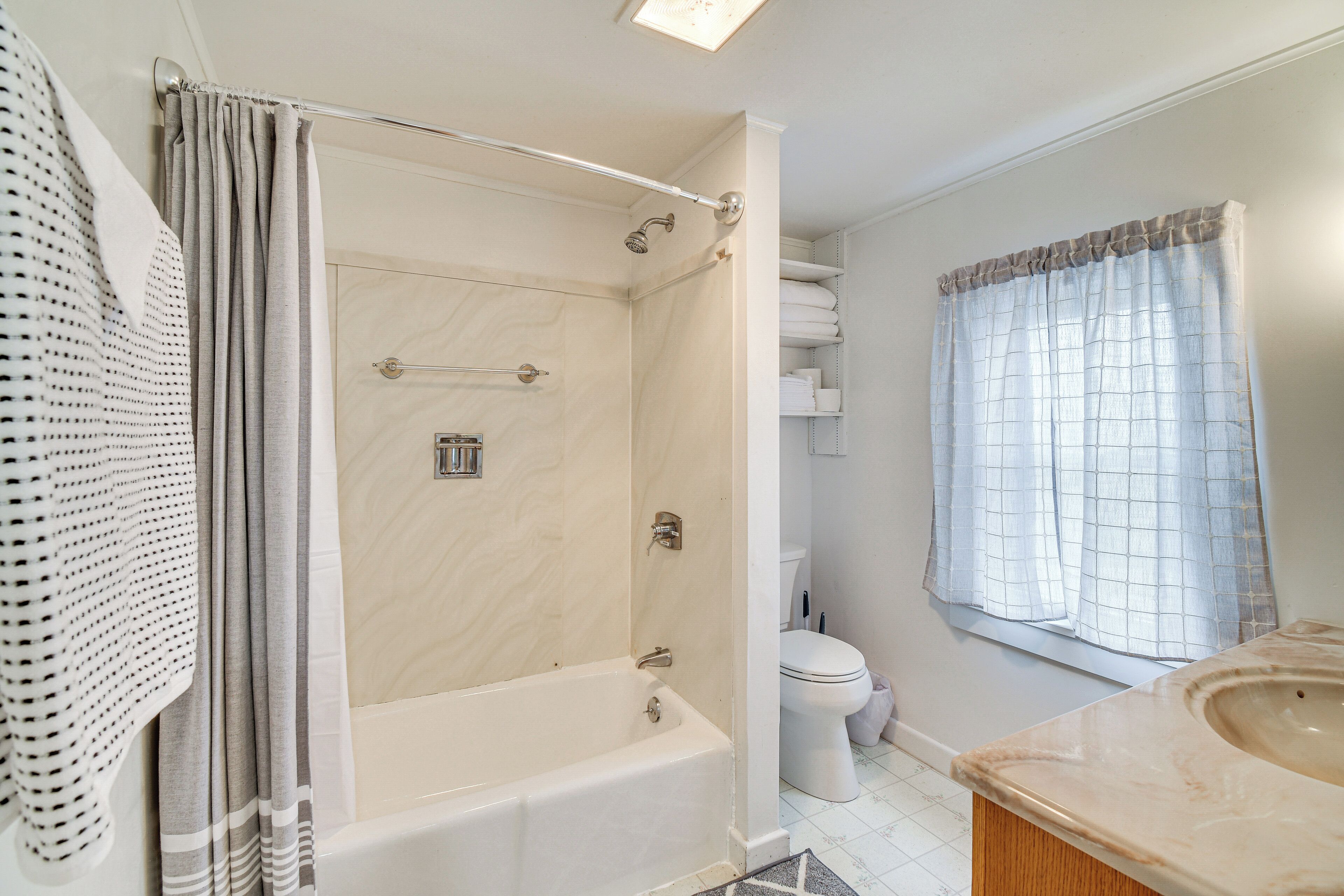 Ein Badezimmer mit Badewanne, Toilette und einem Fenster mit Vorhang.