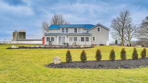 A two-story house with a blue roof, a front porch, and a well-maintained lawn with young trees. - Auburn Finger Lakes Farmhouse w/ Open Views! (Auburn)