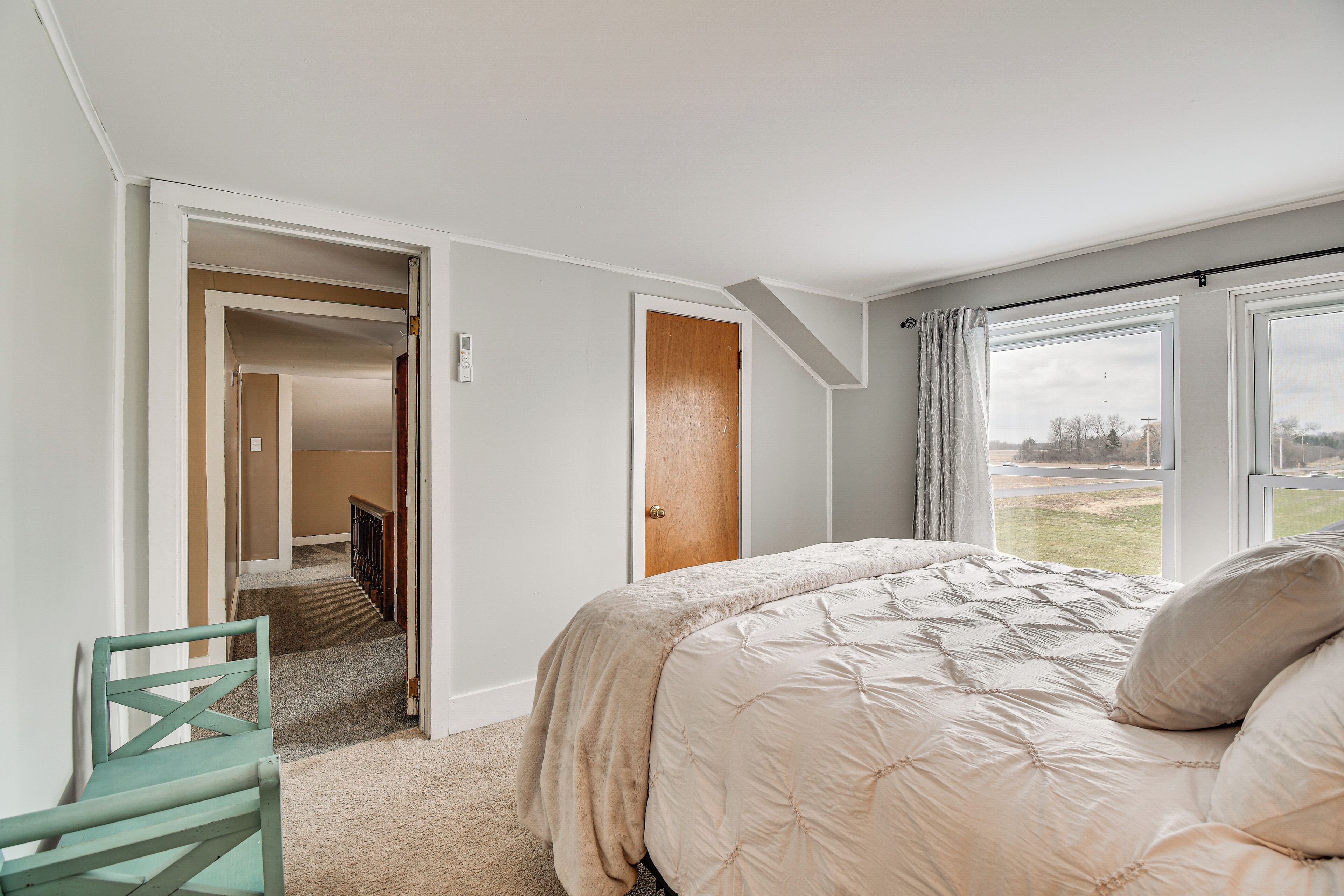 A bedroom with a bed, a chair, a door, and a window.