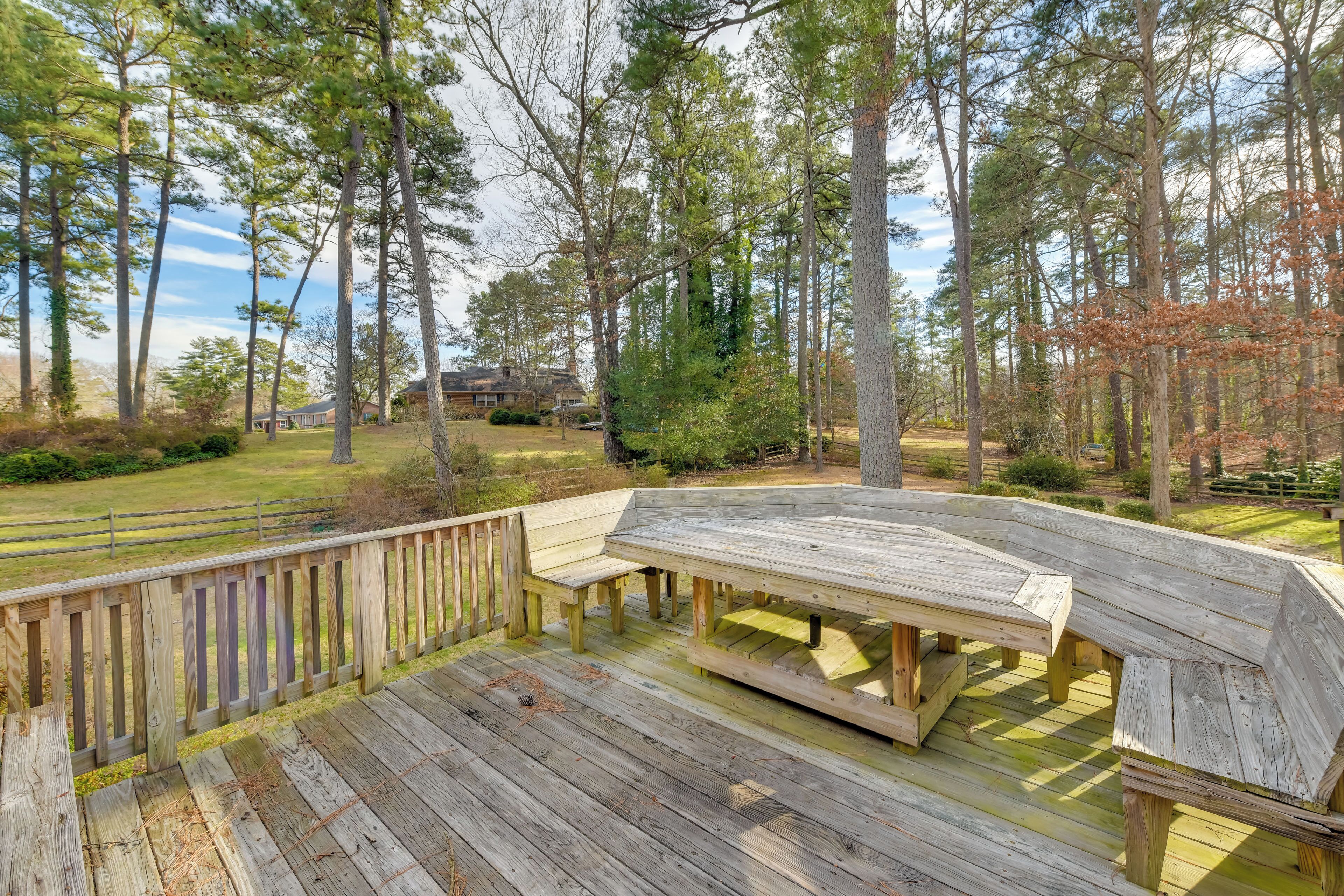 A wooden deck with a bench and table, surrounded by trees and a grassy area.