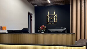 A hotel reception desk with a modern design, featuring a logo above the desk and a potted plant on the counter. - Hôtel Margaux  (Epernay)