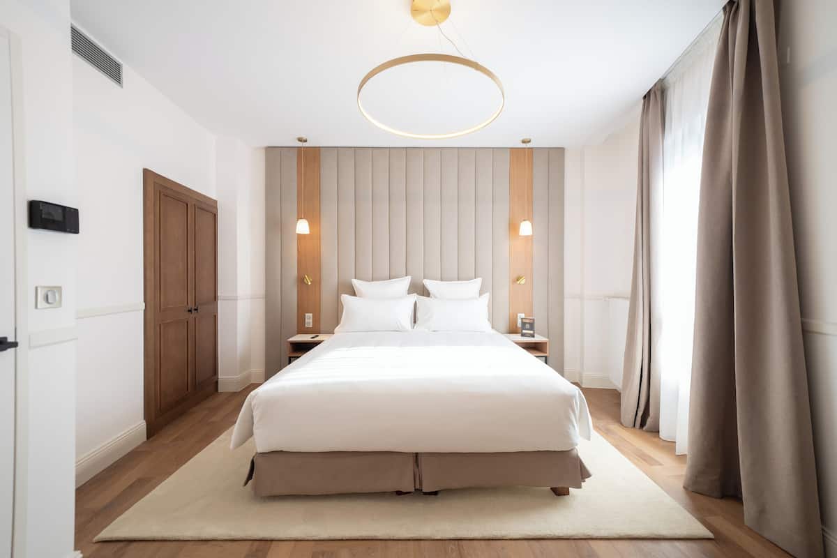 A modern bedroom with a large bed, wooden wardrobe, bedside lamps, and a circular ceiling light.