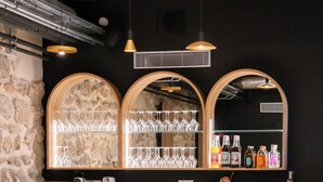 A bar area with a stone wall, wooden bar counter, and seating with round tables and chairs. - Hôtel Margaux  (Epernay)
