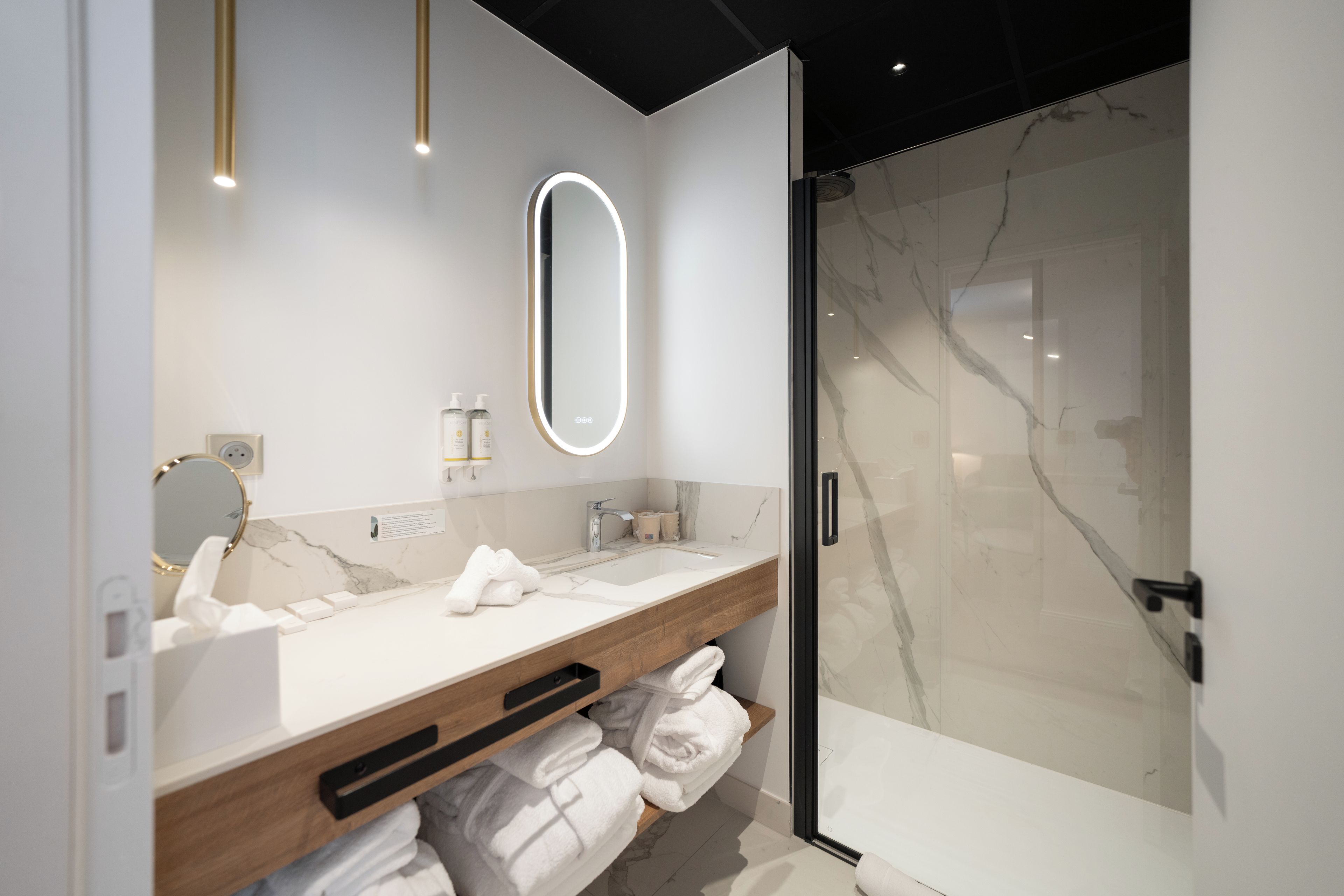 Un bagno moderno con un lavabo in marmo, una cabina doccia in vetro e uno specchio a muro con illuminazione integrata.