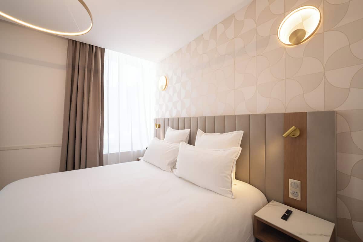 A hotel room with a large bed, a bedside table, a nightstand, and a wall-mounted light fixture.