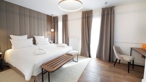 A modern hotel room with a large bed, a wooden bench, a desk, and a chair. - Hôtel Margaux  (Epernay)