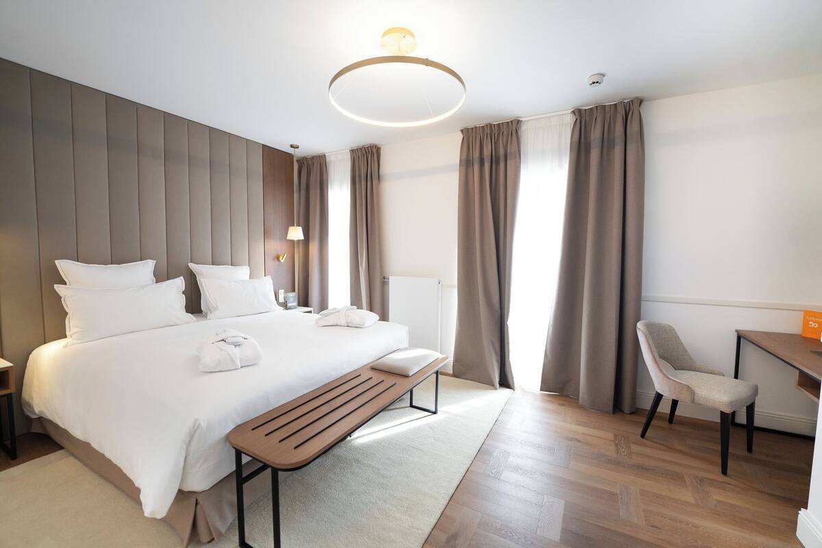 A modern hotel room with a large bed, a wooden bench, a desk, and a chair.