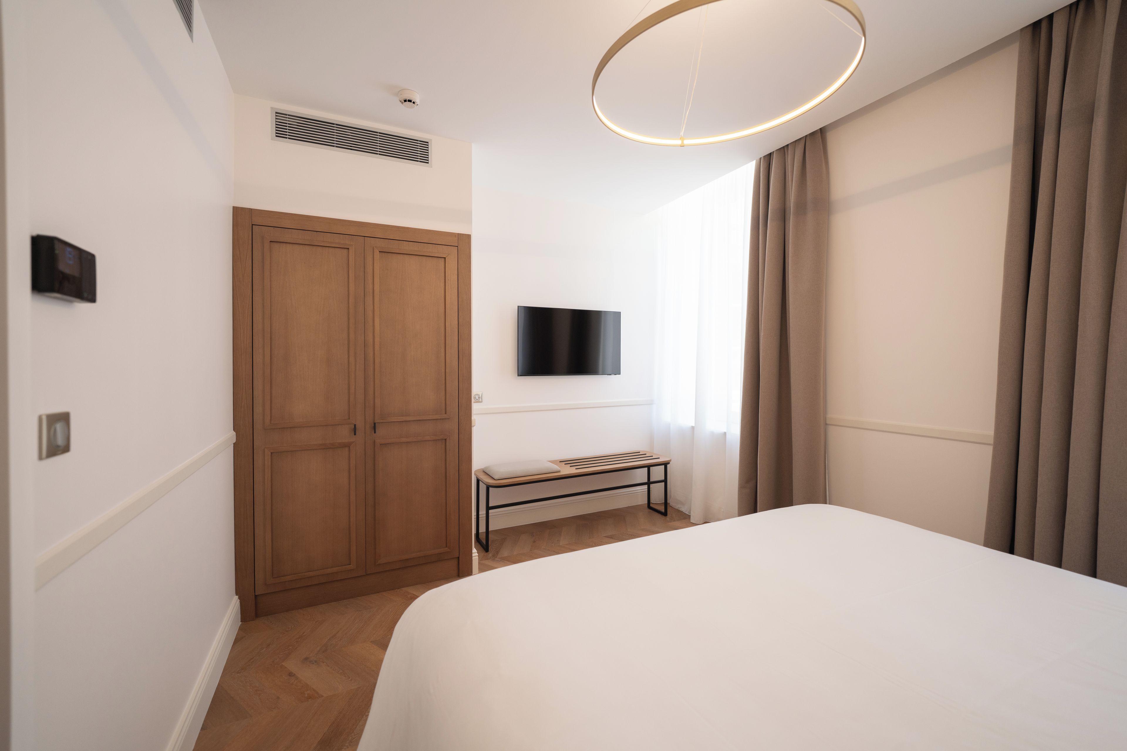 A hotel room with a bed, a wardrobe, a television, and a window with curtains.
