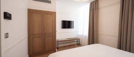 A hotel room with a bed, a wardrobe, a television, and a window with curtains.