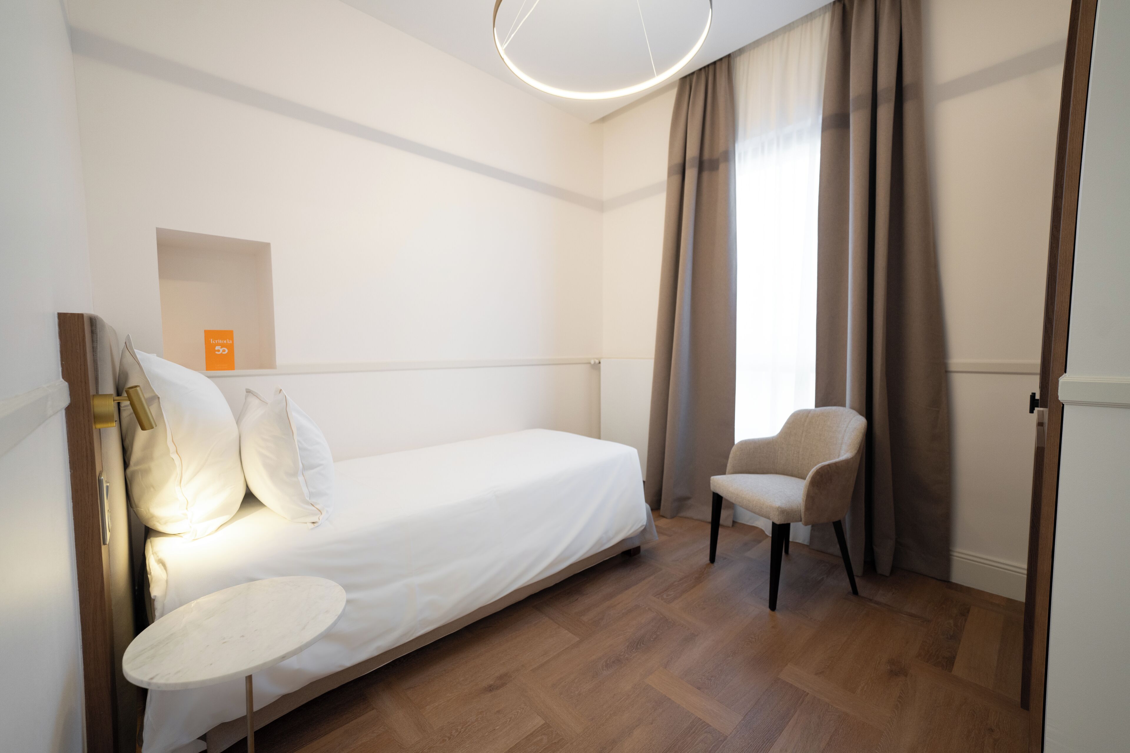 Un dormitorio con cama, una silla, una mesita y una lámpara en el techo.